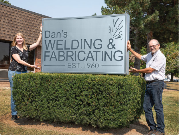 Allison Nielsen and General Manager Bill Myers at the Dan's Welding & Fabricating sign, established 1960